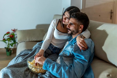 Romantic couple sharing a bowl of popcorn while watching a movie on television in their living room