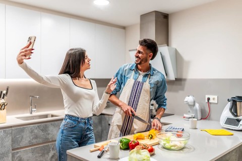 Young couple taking selfie with smartphone while preparing a healthy vegetarian salad in a modern
