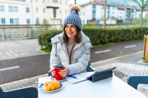 Beauty woman wearing warm clothes and woolly hat warming hands with hot coffee in a sidewalk
