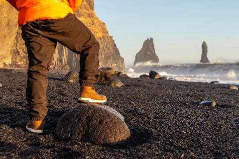 A person is standing on a rock on a beach. The beach is rocky and the sky is blue