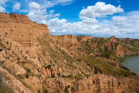 Ein felsiger Canyon mit einem klaren blauen Himmel und weißen Wolken darüber, Barrancas de Burujón,