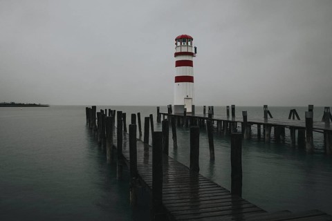 A lighthouse at the end of a wooden jetty under a grey sky over calm water, Podersdorf, Burgenland,