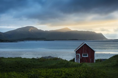 A red wooden hut on the sandy beach of Ramberg (Rambergstranda), with the sea behind it. At night