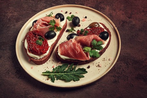 Sandwiches with cheese and prosciutto, dried tomatoes and olives, breakfast on a plate