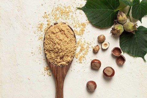 Wooden spoon with hazelnut flour, top view, no people, on a white table