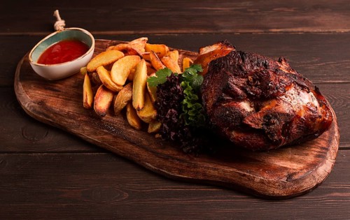 Pork knuckle, in soy-honey sauce, with fried potatoes, on a wooden chopping board, homemade, no