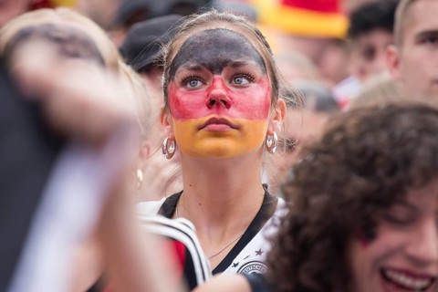 A woman wearing make-up in the German national colours watches the football match in the fan zone