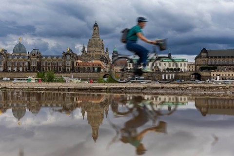 The Dresden silhouette with a cyclist and dark clouds behind the Church of Our Lady is reflected in
