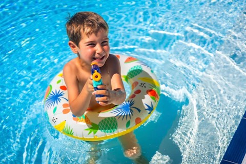 Boy playing with water gun and rubber ring inside the pool