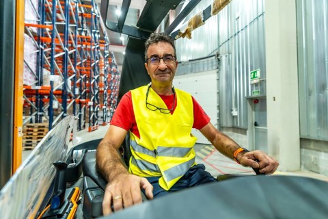 Portrait of a happy mature male worker driving forklift at distribution warehouse