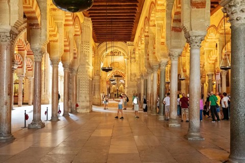 Historic interior with many columns and arches, viewed by people, Cordoba