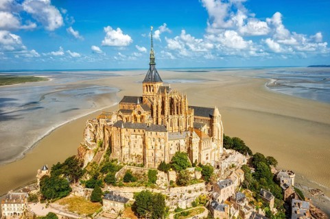 Majestic abbey on an island, surrounded by vast sand, under a clear sky, Le Mont-Saint-Michel