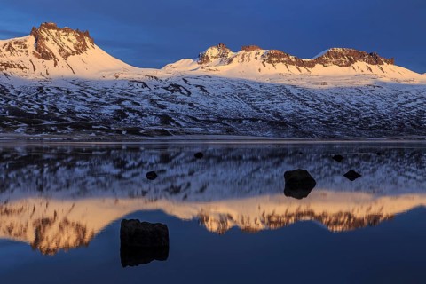 Snow-covered mountains reflected in a fjord in the evening light, Berufjördur, East Fjords,