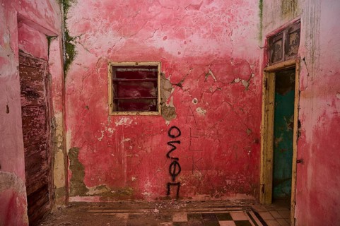 Pink-painted room with graffiti on the walls, exposed to severe decay and ageing due to damaged