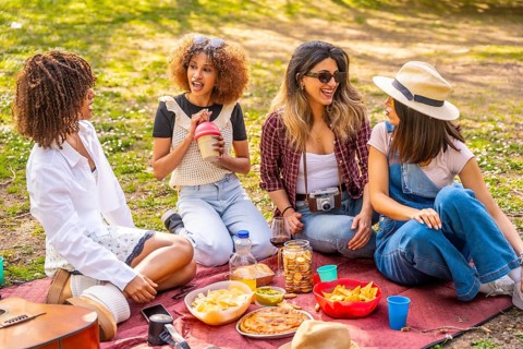 Four female friends enjoying a lively picnic in the park, sharing snacks, laughing, and creating