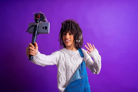 Young latin american content creator waving and recording video with smartphone and external