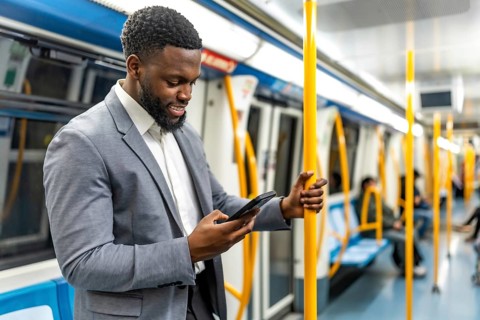 Smiling businessman holding a pole while using a smartphone, standing inside a subway train during
