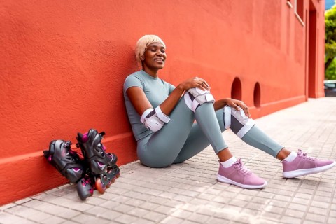 Beautiful african woman roller skating resting sitting on ground and leaning on red facade during