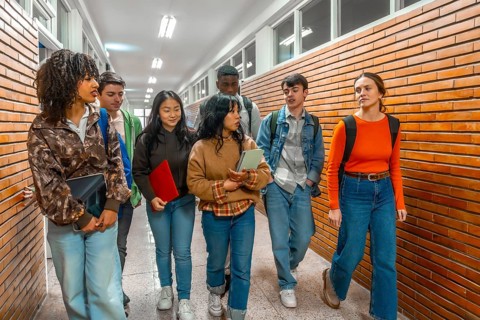 Multi ethnic university students walking down school hallway, chatting and holding books and