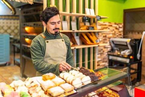 Latin young man arranging sweet artisan pastries on the counter of a bakery shop