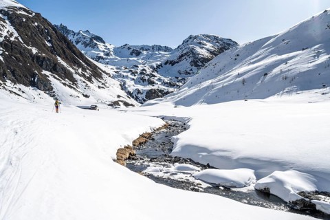 Ski tourer in the snow by a mountain stream in the Funtauna Valley, Graubünden Haute Route, Albula