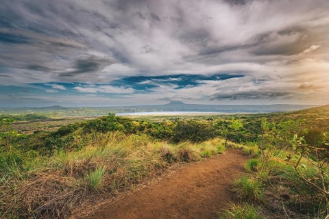 Landscape of a dirt road overlooking Masaya Lagoon. Nature trail overlooking a distant volcano