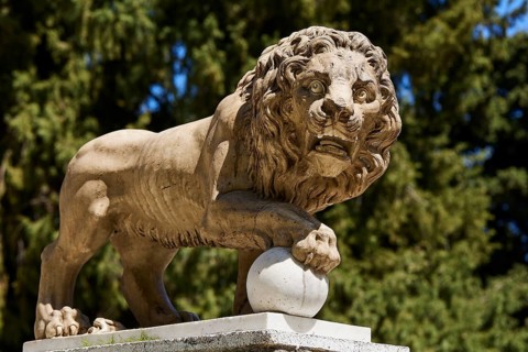 A stone lion statue holding a ball with a forest in the background, Rodini Park, Municipal Park,