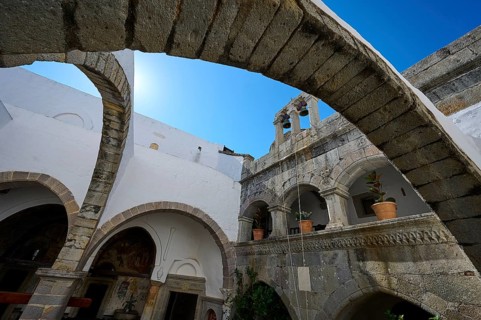 Historic monastery courtyard with stone arches, a tower and hanging plants. Impressive