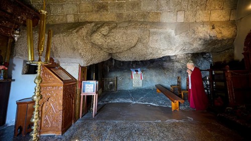 Praying woman in a sacred space with rock walls and an altar, rock grotto, Monastery tis