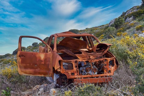 Rusted car amidst blooming wildflowers under a clear blue sky, wrecked car, sky exchanged, Crete,