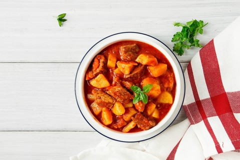 Potatoes stewed with meat, in tomato sauce, with spices and herbs, no people, on a white table