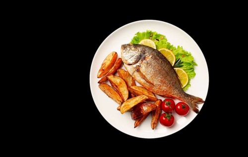 Fried Dorado fish, with potatoes, top view, on a black background, no people