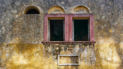 Two old windows in a dilapidated, yellow façade with heavily faded and peeling areas, Italian
