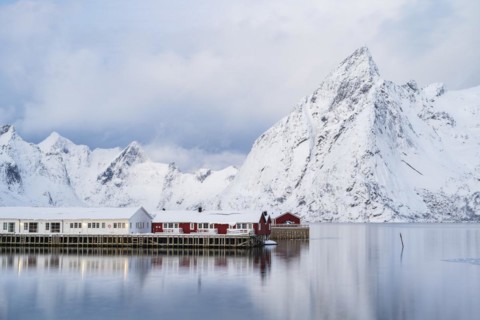 Rorbuer huts of Hamnoy at the fjord, snowy mountains in the background, Hamnøy, Reine, Moskenesøya,