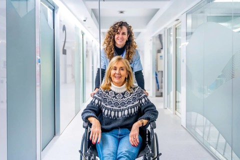 Happy nurse carrying mature female patient in wheelchair at the hospital corridor