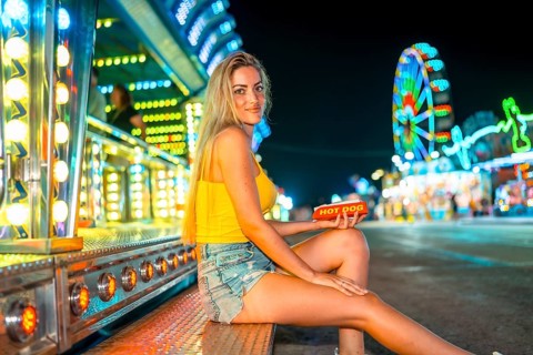 Side view photo of a blonde woman holding an unhealthy hot dog in a night fair