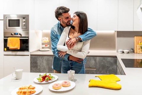 Young loving couple hugging and laughing in contemporary kitchen, with croissants, strawberries,