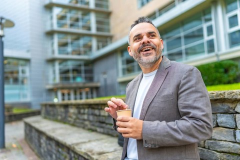Happy mature caucasian businessman enjoying coffee break outside the block office in the city