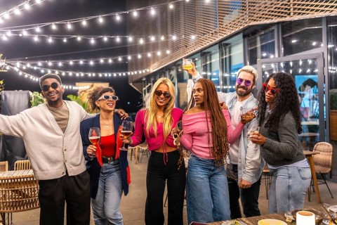 Group of young diverse multi-ethnic friends having fun at bar terrace decorated by lights at night