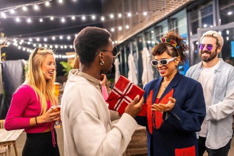 Multi-ethic friends giving a gift box to a woman celebrating birthday in the terrace of a modern