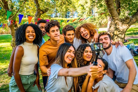Smiling multi-ethnic friends taking selfie with wearable camera at park while celebrating birthday