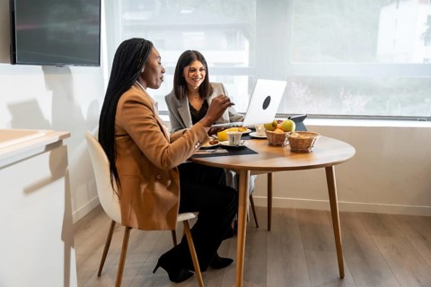 Two businesswomen having breakfast and working on a laptop in their hotel room during a business