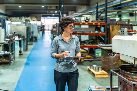 Female caucasian manager of a metallurgic cnc factory doing inventory holding a clipboard walking
