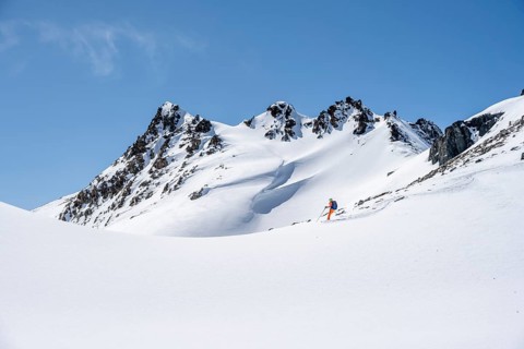 Ski tourer on the descent, minimalist winter landscape, white snow and dark mountains on the