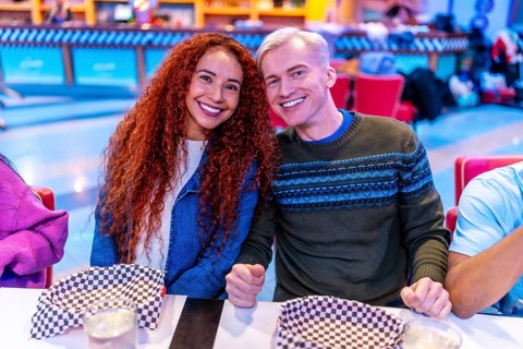 Young multiethnic friends enjoying a meal together at a bowling alley restaurant, celebrating their
