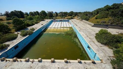 Abandoned swimming pool with algae-infested water, graffiti and concrete walls, surrounded by