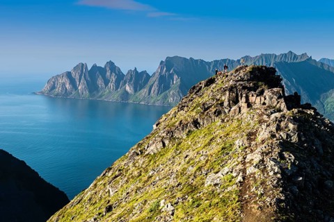 Hikers on top of Mt. Husfjell, view to mountain range Okshornan in the back, peaks rising from sea