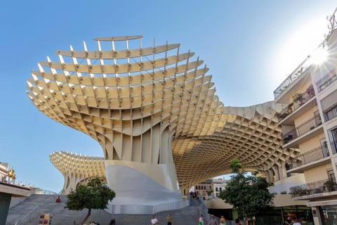 Imposing wooden construction of the Metropol Parasol in strong sunlight between city buildings,
