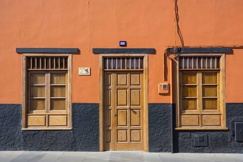 A building facade with an orange wall, wooden door, and windows. The base is painted black,