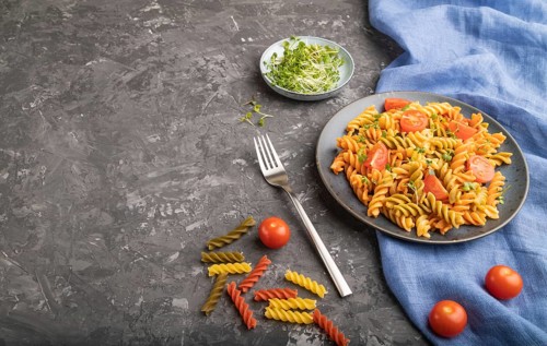 Tortiglioni semolina pasta with tomato and microgreen sprouts on a black concrete background and